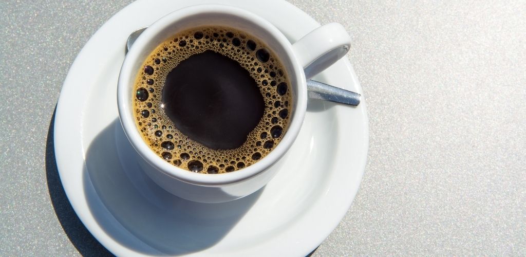 A white cup of black coffee on the table.