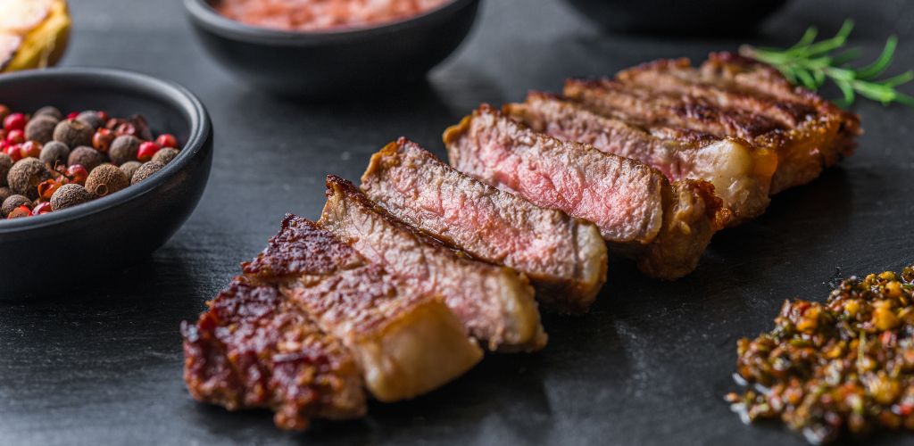 New york strip loin beef steak meat with chimichurri sauce against black stone background