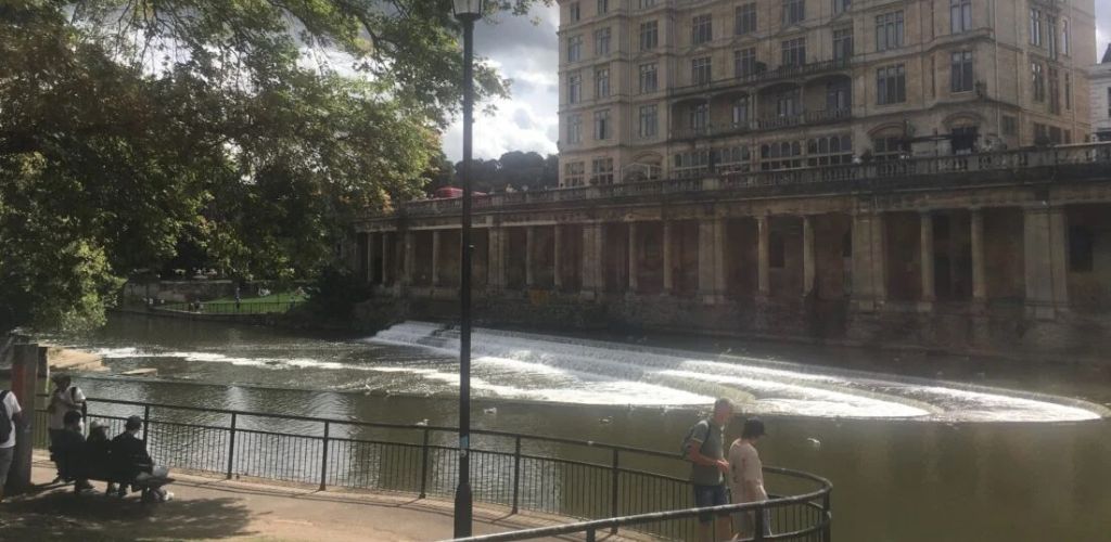 A lake and an old building on the right, and people staring at the lake on the left. 