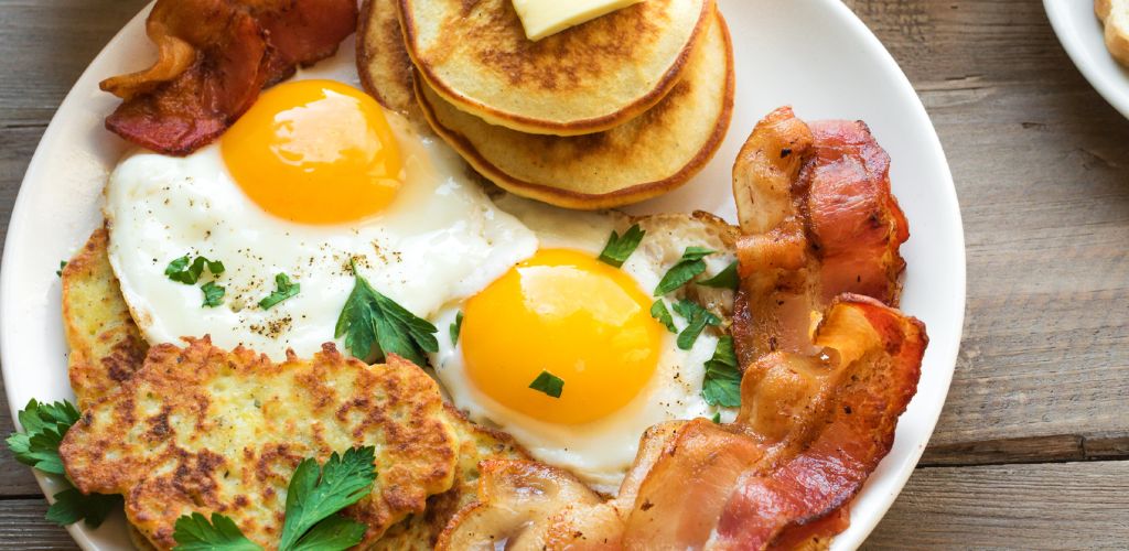 Full breakfast on wooden, top view. Sunny side fried eggs, roasted bacon, hash brown and pancakes.