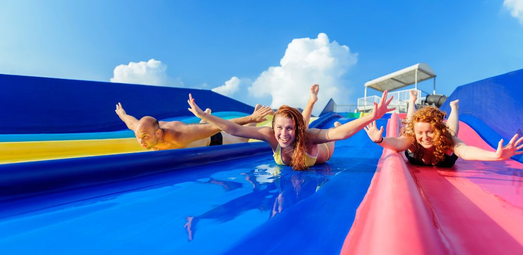 Three friends on the water slide raise their hands. 