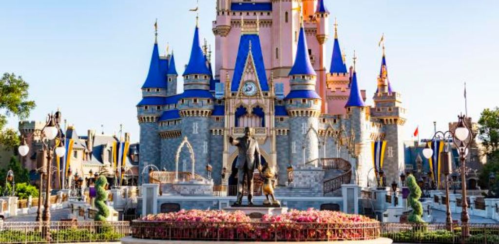 Disney castle and a statue at the center and garden. 