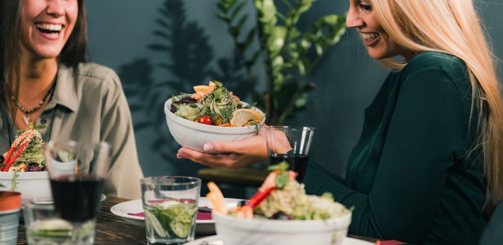 Restaurant for vegetarians. Female friends having fun while eating a fresh salad in a restaurant. 