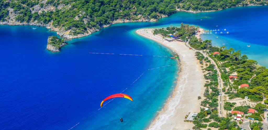 A beautiful blue beach and Island with green trees and one paragliding at the air.
