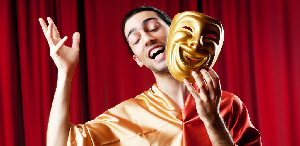 A man on stage with a wide smile and a gold mask smiling.