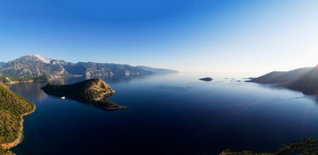 At sunset, a blue sea surrounded by green mountains and a small island in the centre. 