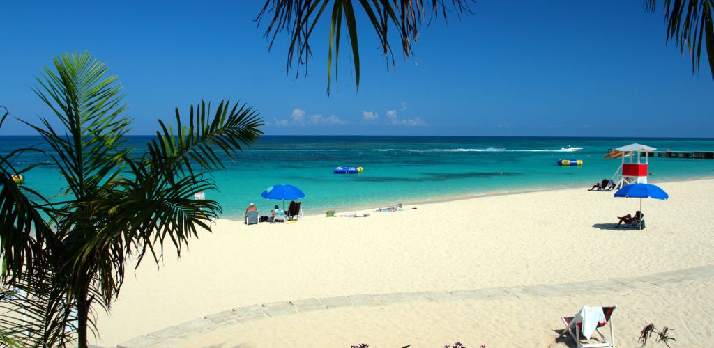 A beach with white sand.  Two modest beach tents and four people sunbathing on the beach. 