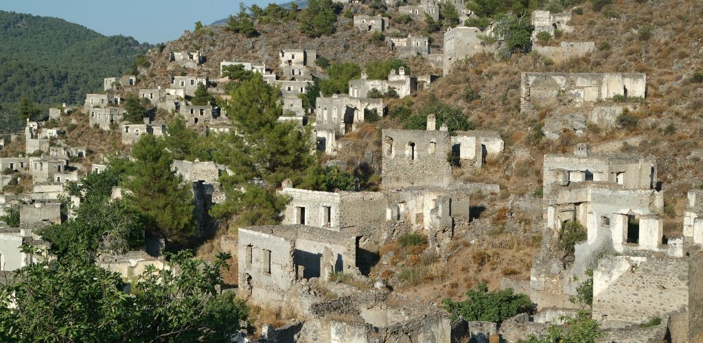 An uphill with abandoned houses structures and surrounded by trees and dried grass. 