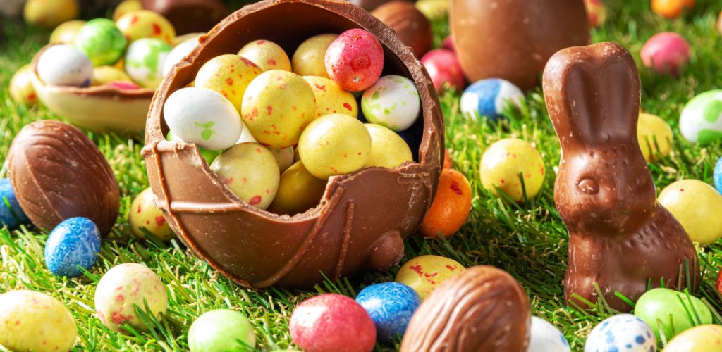 Easter egg hunting background. Various candy and chocolate Easter eggs, bunnies, and rabbits with baskets for eggs on the green park or garden background.