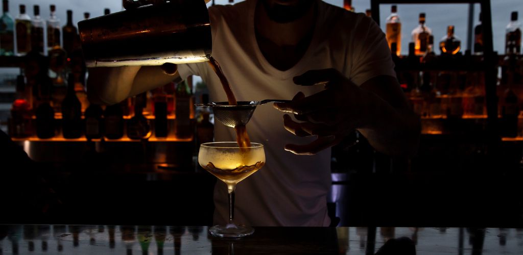 A bartender prepares a cocktail at the bar counter. 