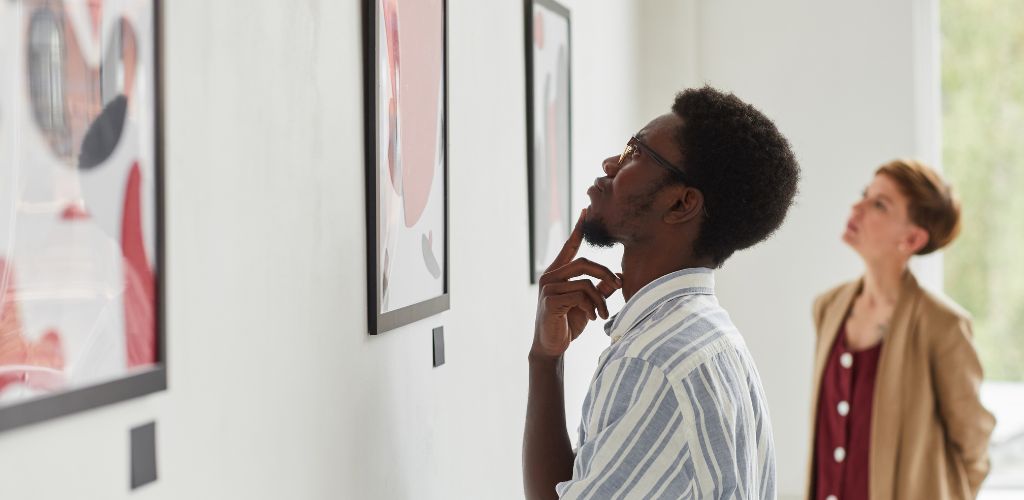 A man and a woman looking at a painting on the wall. 