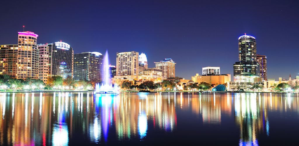 Orlando's downtown skyline panorama over Lake Eola at night with urban skyscrapers, fountain, and clear sky. 