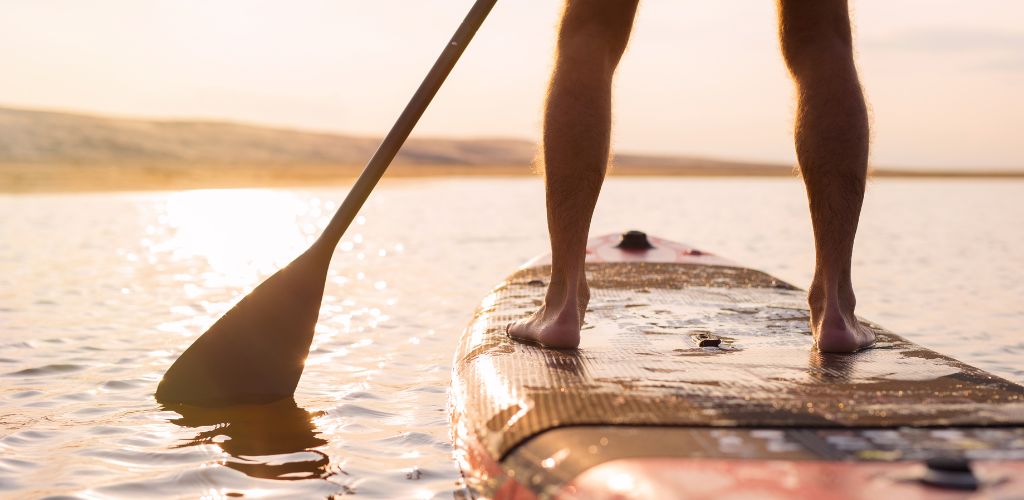 A man standing on a padding board in the sunset. 