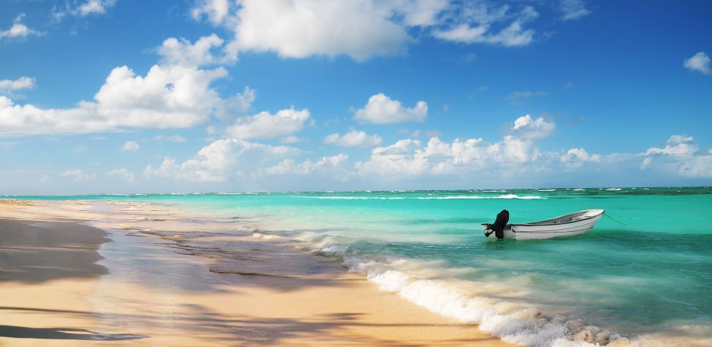 A white beach sand and a wavy sea and one small boat on the shore. 