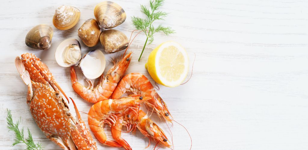 Assorted seafood consisting of shrimp, crab, and clams with lemon and dill on the side.