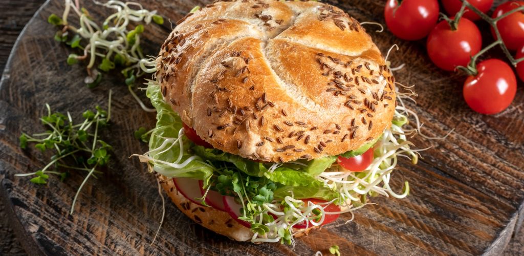 A healthy and delicious Sprout Burger with tomato on the side on a wooden plank