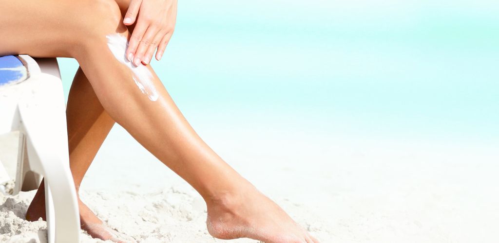 Sunscreen/suntan lotion. Woman putting sun screen lotion on sexy legs on beautiful beach on summer holidays.