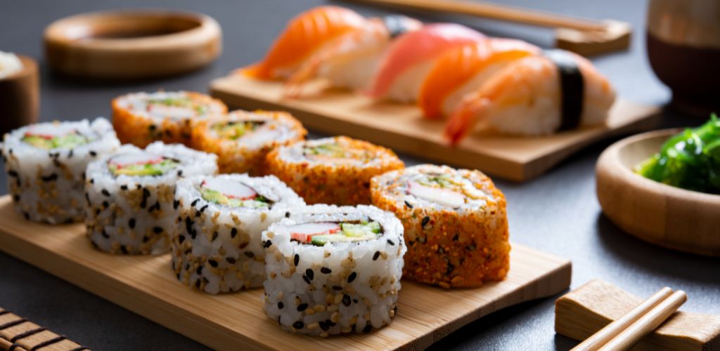 Sushi set uramaki and spicy sushi rolls served on  bamboo tray. Various kinds of sushi pieces served on black slate with wooden chopstick. 