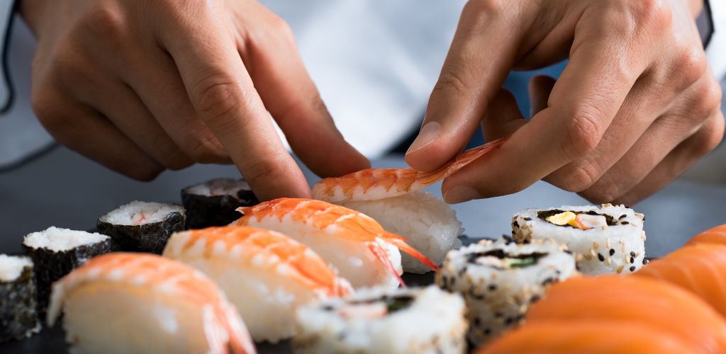 Closeup of man hands preparing Japanese sushi served on a black stone plate.