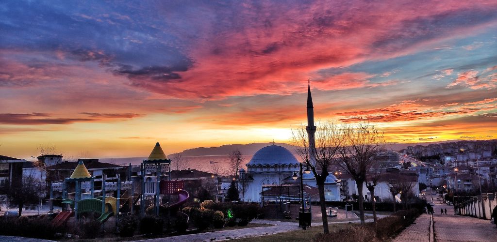 A play ground, mosque, street, and other building structure under the sunset. 