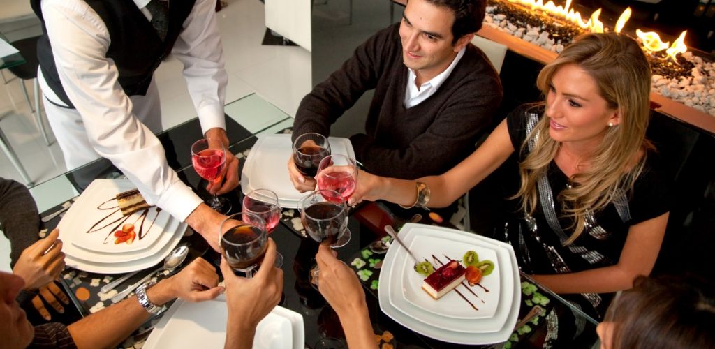 A group of people are enjoying dinner at a restaurant and toasting a glass of cocktail given by a waiter. 