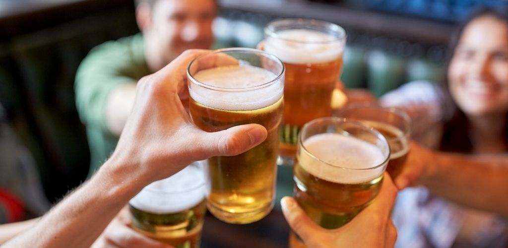 A group of a mix of girls and boys enjoying and toasting a glass of beer.