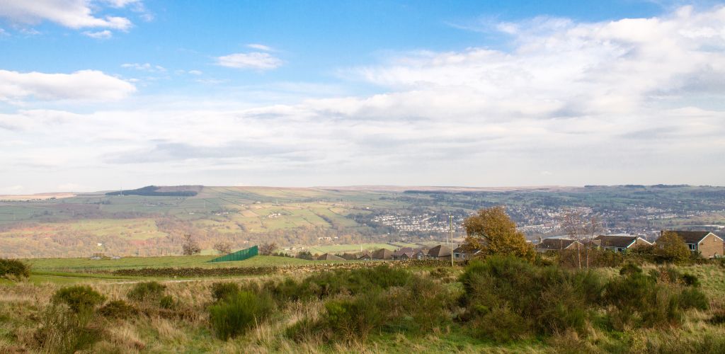 West Yorkshire hills, a green field, homes, and a foggy sky.