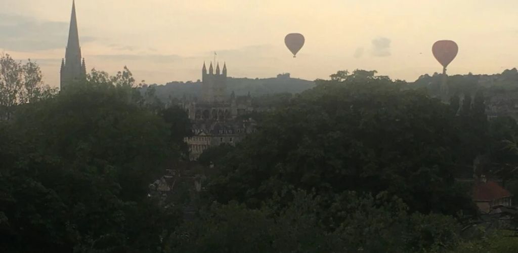 A historic castle surrounded by green trees and a air balloon above the castle. 