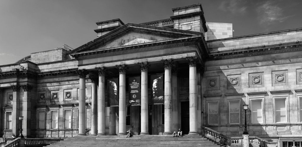 A black-and-white view of the famous World Museum and three individuals sitting on the museum's stairs.