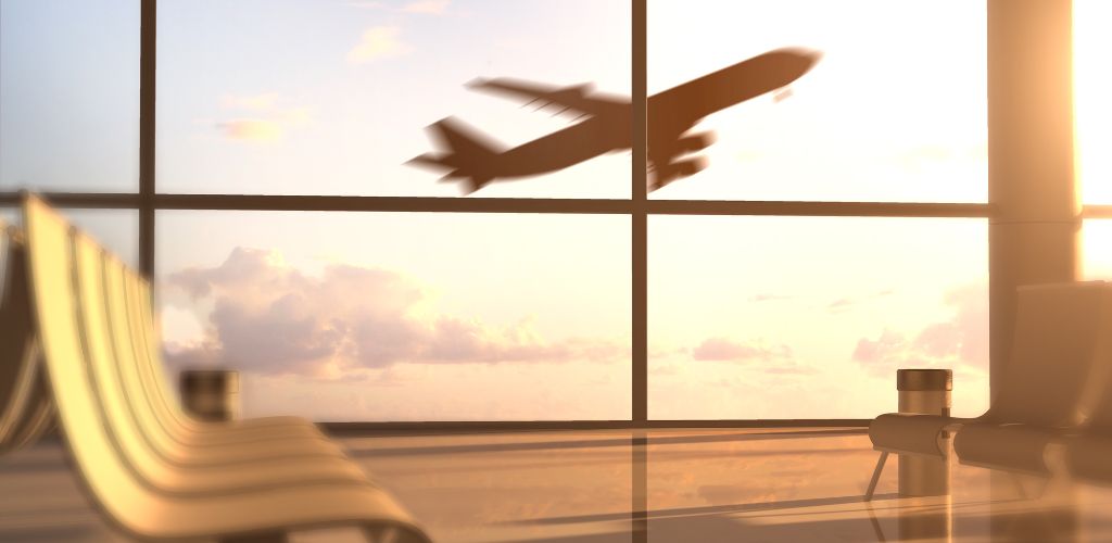 A waiting area inside the airport with a takeoff airplane visible through the large window. 