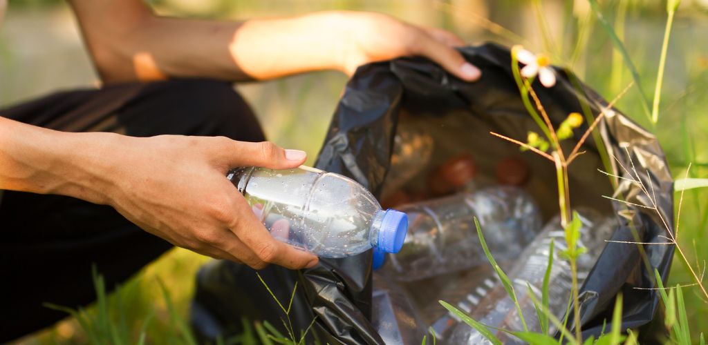 A hand of a person holding a plastic bottle and put into black trash bag. 