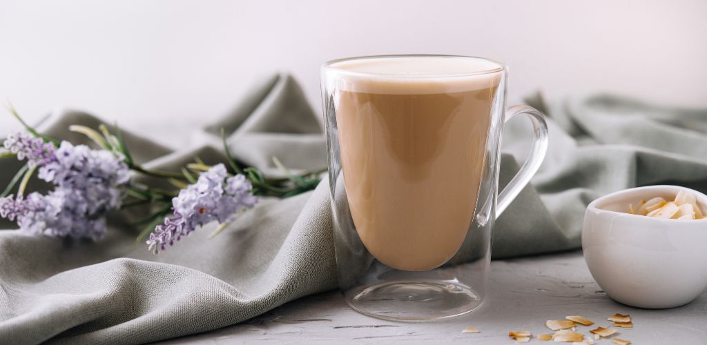 Almond milk latte in a glass and flower at gray fabric on the background. 