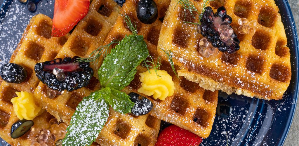 Waffles on a Plate with blueberry, strawberry, and green garnish on top. 