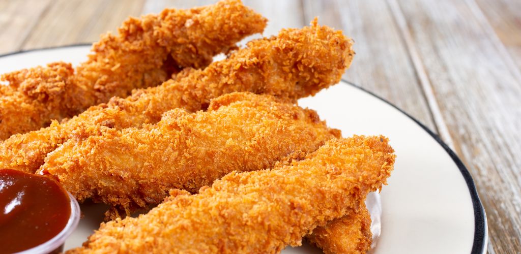 A view of a plate of breaded chicken finger and a ketchup on the side. 