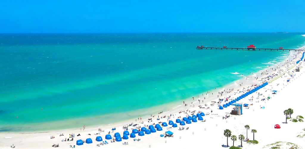 Clearwater Beach Florida with blue tents and tourists on the shore. A pier at the far sight. 