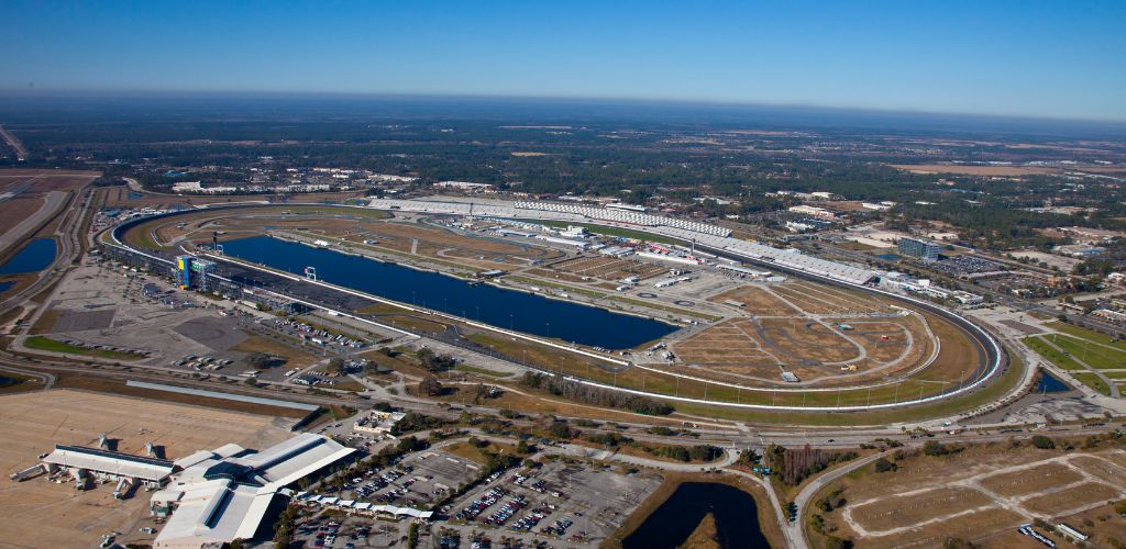 Aerial view of the racetrack, with grassy fields surrounding it, a parking lot, and little lakes. 
