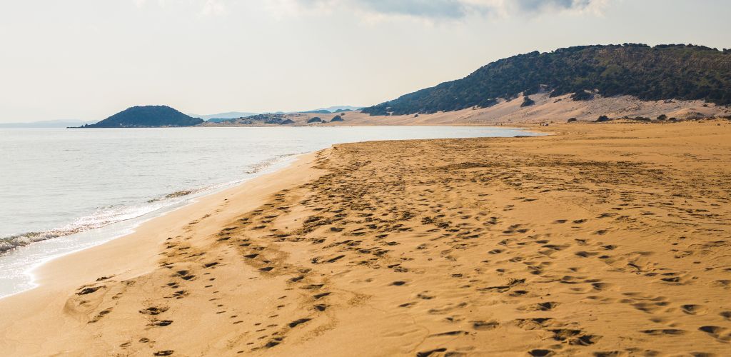 A clear sea, golden sand, and a green mountain in the distance. 
