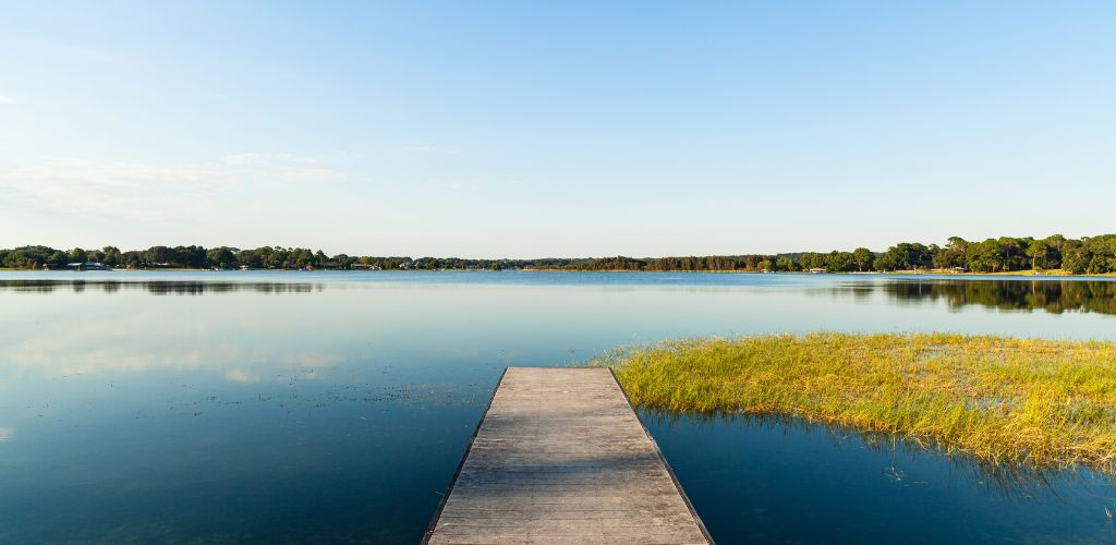 A bridge towards to a beautiful lake surrounded by green trees. 