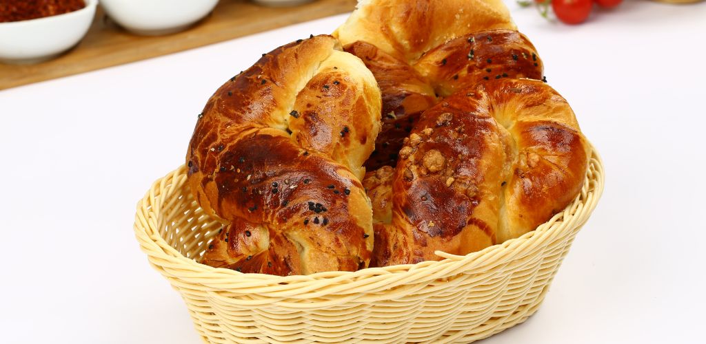 A basket of three pieces of bread formed like an infinity on a white table. 
