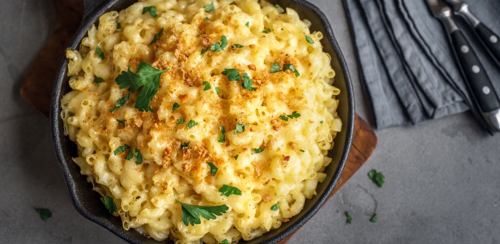 Mac and cheese, American style macaroni pasta with cheesy sauce and crunchy breadcrumbs topping on concrete table, top view.