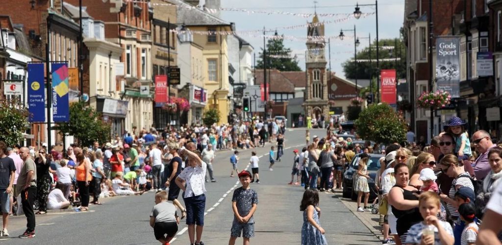 In Newmarket Cambridge, there are many tourists on the street and a market on both sides of the street.