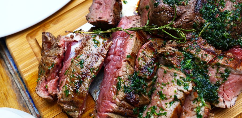 Close up a big portion of sliced grill roasted beef chateaubriand tenderloin meat with thyme and herbs served on wooden cutting board, high angle view. 