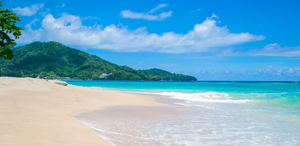 A day picture of a clean beach, white sand, clear water green mountain at the far sight. 