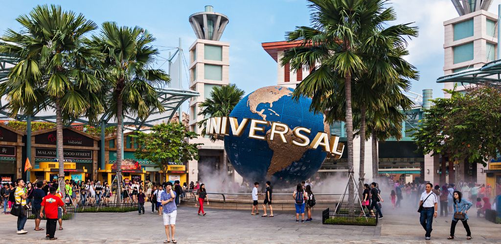 A globe statue with the word "Universal Studios" imprinted on it during a crowd of tourists. 
