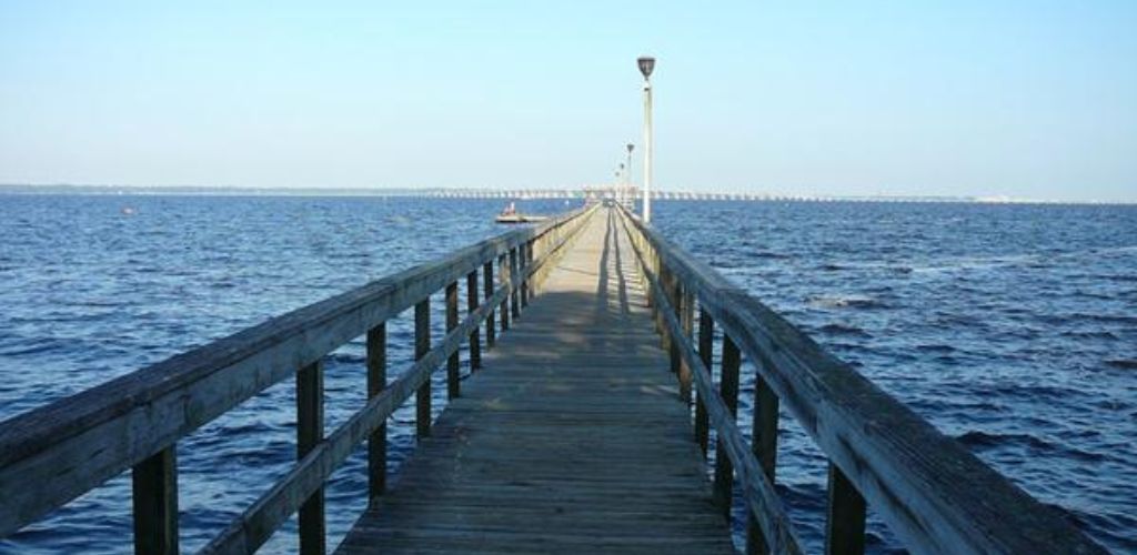 A long bridge leading to a vast sea, with a pole light on the side. 
