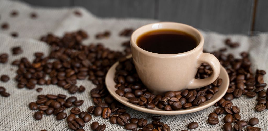 Coffee cup with roasted coffee beans on linen background. Mug of black coffe with scattered coffee beans. Fresh coffee beans.