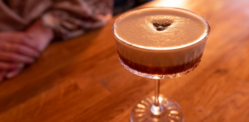 An espresso martini in a crystal glass on a wooden table on a bar. 