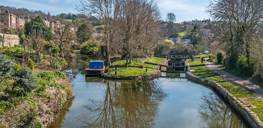 A walkway on the right side of a canal with water gates and trees surrounding it. 