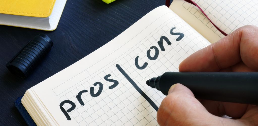 A man is writing pros and cons. On a black wooden table, on a grid ling notepad. 