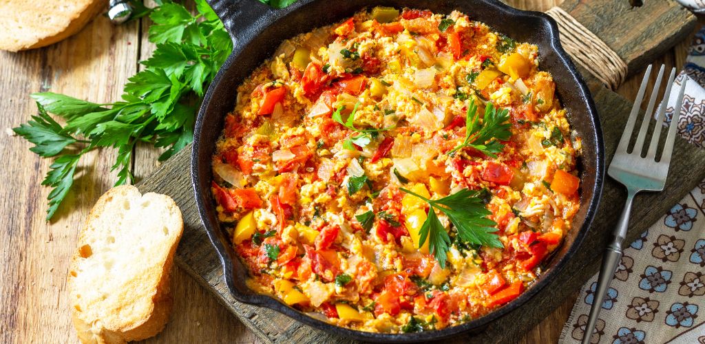 Traditional Turkish dish. Fried vegetables with scrambled eggs in a cast iron frying pan on a wooden table. 